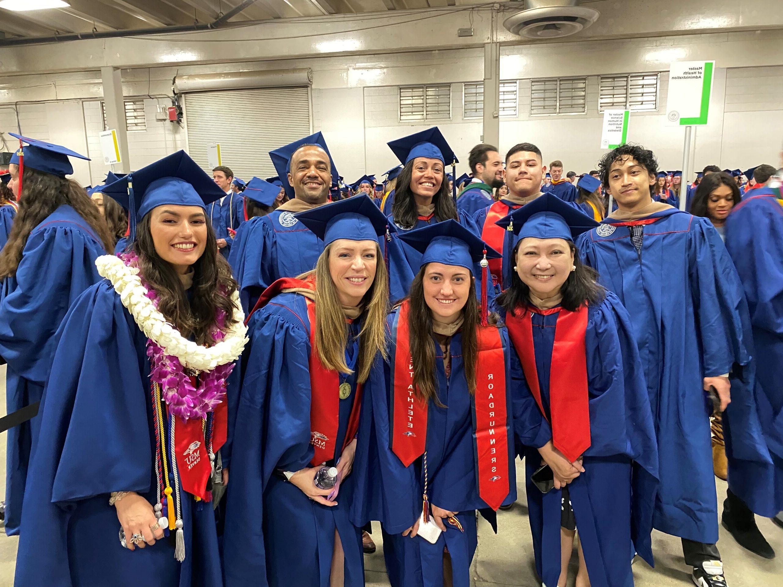 Spring 2024 Commencement - 8 MPAcc students smiling in graduation regalia as they are waiting to line up and enter the coliseum main floor